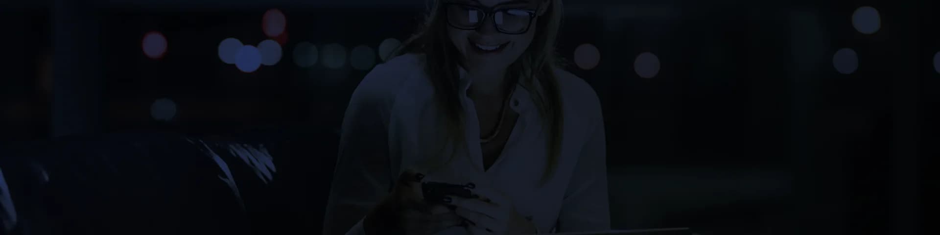 imagem de fundo abstrata no ton azul escuro com uma mulher branca, loira de blusa branca, sorrindo enquanto utiliza o celular